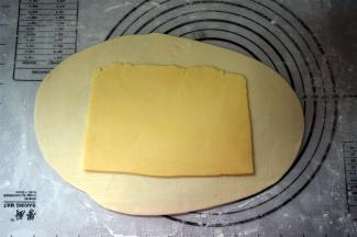 揉面垫上撒点高筋粉防粘，将松弛好的水油皮擀成油酥面积的两倍，将油酥皮放在中间。