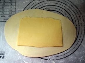 揉面垫上撒点高筋粉防粘，将松弛好的水油皮擀成油酥面积的两倍，将油酥皮放在中间。