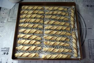 左手固定住面条的一端，右手提着另一端扭几圈，放入烤盘中。