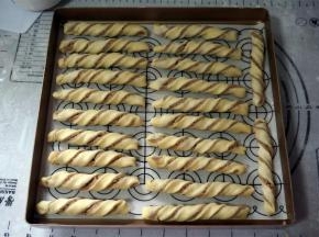 左手固定住面条的一端，右手提着另一端扭几圈，放入烤盘中。