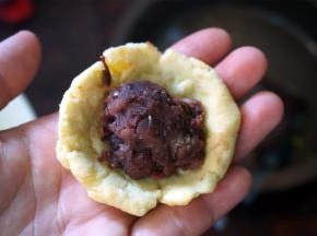 取一小块面团，按扁，放入馅料，团成小球。