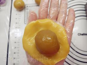 取出一个月饼皮剂子，将其压扁，在饼皮中间放上馅料。翻过来，将皮收一下，让它紧贴着馅料。