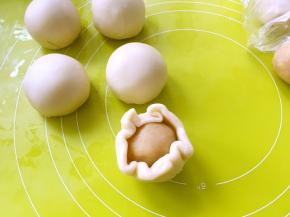 之后压扁，擀成大一些的薄片，包裹上莲蓉蛋黄球，收好收口，收口朝下放