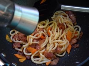 然后加入乌冬面、培根炒匀，磨入黑椒碎