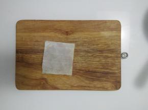 放上第二张馄饨皮，用手从中间往四周按压，把肉馅压匀压平，四周粘紧。