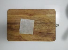 放上第二张馄饨皮，用手从中间往四周按压，把肉馅压匀压平，四周粘紧。