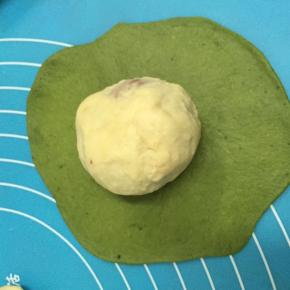 取一绿色面团，擀成圆形，包住以上白面团，捏紧收口，揉圆，放至烤盘中。