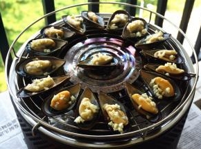 烧烤炉起炉火后，将海虹排放到烤网上，给每一个海虹抹油并撒上蒜粒。