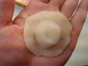 取一个白色水油皮放在手心按扁，包入一块油酥；