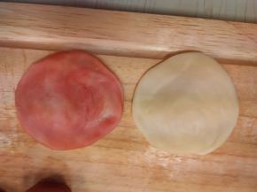 分别将白色、红色水油皮卷竖在案板上，按扁；用擀面杖擀成圆片；