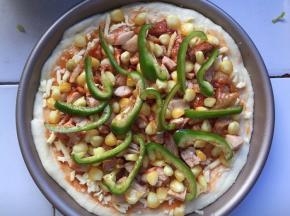 烤盘中放入马苏里拉芝士，将鸡腿肉切成小块放入披萨盘中，放入青椒和玉米
