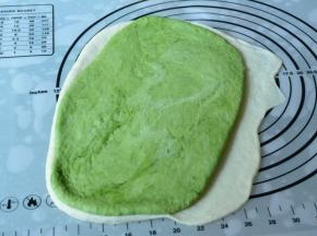 抹茶面团也擀成一张小于白面皮的面皮，铺在白色面皮上。