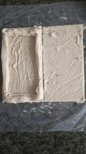 把四边形一分为二，其中一半用剩下的边料把四边围起来。中间用叉子戳一些孔，放入苹果馅。