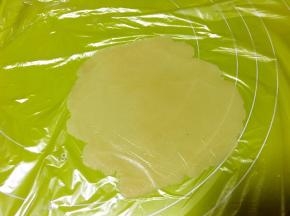 冰箱取出月饼面团，取15克一份面团，盖保鲜膜用擀面杖擀成圆片，中间厚四周薄一点