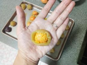 取一个莲蓉球在掌心中按扁，包入一个蛋黄，利用虎口慢慢收好口