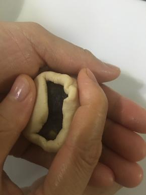 把桃山皮放在手掌压扁，馅料放在桃山皮中间，慢慢推动桃山皮，慢慢转动手，使饼皮慢慢上爬，收口并再次搓圆