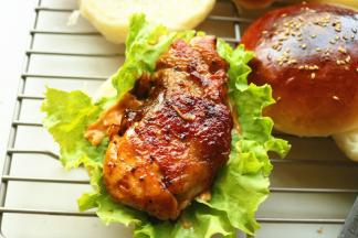 剖开的汉堡上铺上生菜叶子，抹上千岛酱，再放上剪好的鸡腿，盖上另一片，汉堡就做好了。