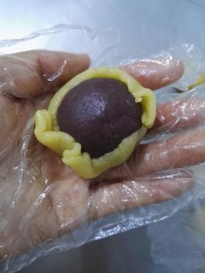 10、将一个红豆馅慢慢的包入面片中，然后用手指将面皮慢慢地向上推，将红豆馅全部包上。