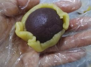 10、将一个红豆馅慢慢的包入面片中，然后用手指将面皮慢慢地向上推，将红豆馅全部包上。