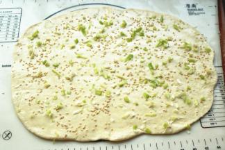 取一个面团，擀开成长方形的面片，抹上一层花生油，撒葱末、盐和炒香的白芝麻。