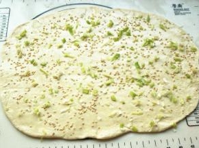 取一个面团，擀开成长方形的面片，抹上一层花生油，撒葱末、盐和炒香的白芝麻。