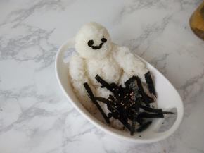 取一个有深度的碗或盘，将米饭大白放入，并将海苔剪成细条，并剪出大白的脸部眼和嘴巴，洒上少许熟芝麻。