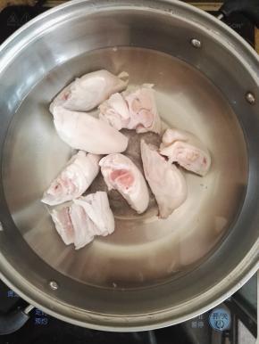3、猪蹄清洗干净，开火锅中倒入水，加入猪蹄焯煮，加入白酒，去除焯出的血沫，再用凉水清洗猪蹄。