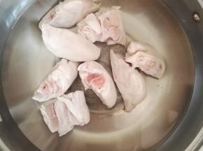 3、猪蹄清洗干净，开火锅中倒入水，加入猪蹄焯煮，加入白酒，去除焯出的血沫，再用凉水清洗猪蹄。