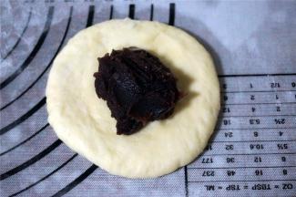 取一个面团，压扁，放入豆沙馅包裹好，收口朝下。