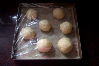 排气后，揉成长条，然后切分成7等份（称量总重后平分7份哦），揉成小圆球，平均摆放在烤盘上，并喷上少许清水，盖上保鲜膜。