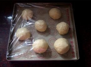 排气后，揉成长条，然后切分成7等份（称量总重后平分7份哦），揉成小圆球，平均摆放在烤盘上，并喷上少许清水，盖上保鲜膜。