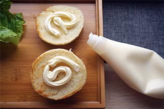 取出一个汉堡包坯，给两个煎面都挤上色拉酱。