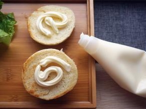 取出一个汉堡包坯，给两个煎面都挤上色拉酱。