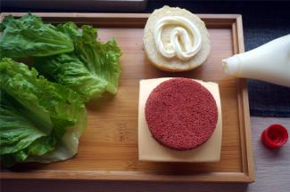 然后从底部往上组装汉堡，顺序是面包底，红丝绒蛋糕片，芝士片，红丝绒蛋糕片，生菜，面包面。