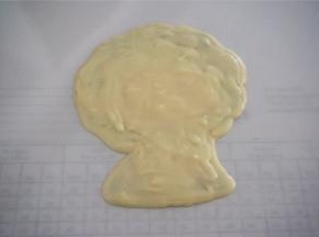 然后脸部填上水蜜桃颜色巧克力，嘴巴和衣服用红色巧克力填上，其余用白色巧克力填上，最后白色巧克力覆盖转印整体，放入冰箱冷冻至硬。