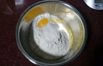 将高筋粉放入深盆中，打入一只鸡蛋，用筷子搅拌一下。