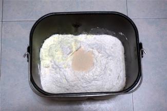 然后加入高筋粉，在其中一个角放入奶粉。中间挖空放入酵母。