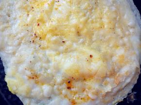 待鸡蛋表面八成凝固了，用锅铲将饼边缘与锅底稍分离，拎起两边，迅速翻面后，在上面刷调好的甜面酱和辣椒酱