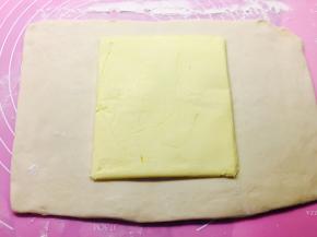 取出冷冻的面团，擀成长方形，将黄油片放置在中间位置，两头向中间折叠。以接口位置在中间为宜。接近借口位置。上下两边要封口捏紧。