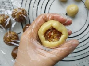 取一个饼皮，按扁后放上馅料。两只手配合，用虎口把饼皮往上推。整理好收口，搓圆。