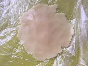 冰箱取出松弛好的月饼面团，取15克一份，包裹上保鲜膜擀成中间厚四周薄的圆片