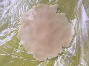 冰箱取出松弛好的月饼面团，取15克一份，包裹上保鲜膜擀成中间厚四周薄的圆片