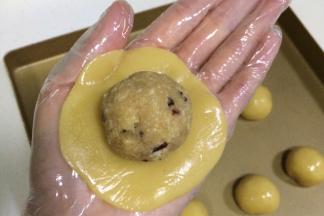 取一份饼皮面团，放在掌心，用另一只手轻按压面团，拍成圆饼状，放上一份蔓越莓椰蓉馅。