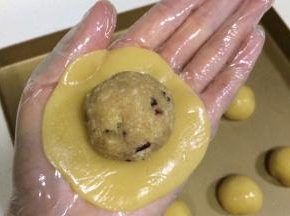 取一份饼皮面团，放在掌心，用另一只手轻按压面团，拍成圆饼状，放上一份蔓越莓椰蓉馅。