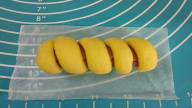 将面团绕着火腿上放在油纸上。（卷时要留一点间隙）