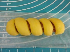 将面团绕着火腿上放在油纸上。（卷时要留一点间隙）