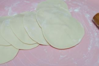 把清水和酵母粉先放进小盆里混合均匀，再把面粉放进去，混合均匀后放置揉面垫上，揉成一个光滑的面团，再分成若干个小面团，揉圆后擀开，擀成四周薄，中间厚的圆面片，就是包子皮了。我这里用的是一次发酵法。