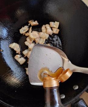 5、当五花肉被煸得吐油时，加入料酒。