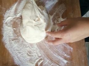 面团用筷子挑到撒满了面粉的面板上。粘上面粉面团就不粘手了