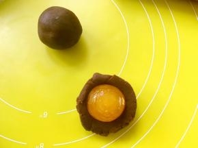 将豆沙馅分成8等份，取一份压扁，包裹上咸蛋黄，收好收口